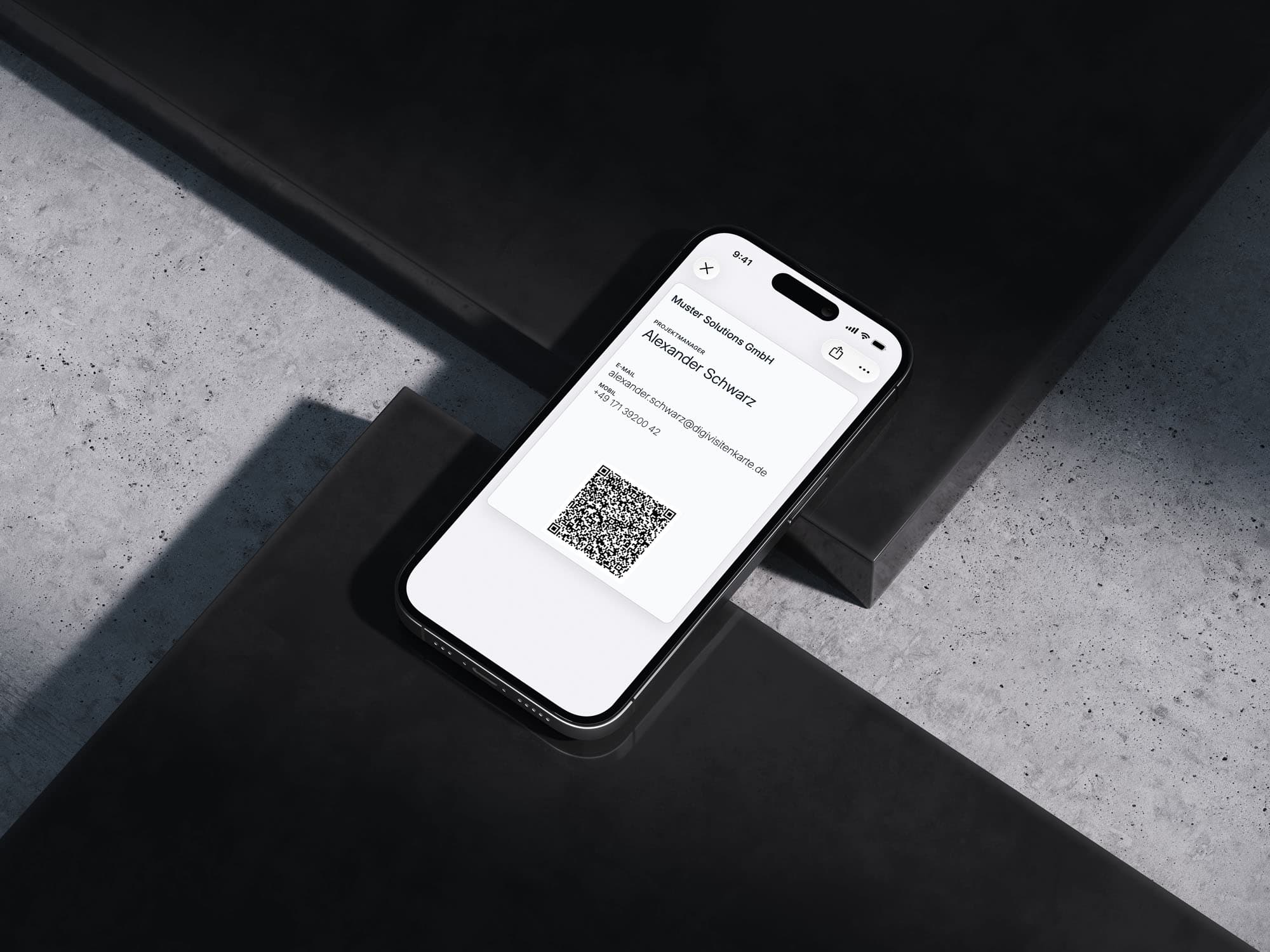 Ein iPhone liegt angewinkelt auf dunklen Betonstufen und zeigt eine cremeweiße digitale Visitenkarte im Apple Wallet: Muster Solutions GmbH, Projektmanager Alexander Schwarz, mit E-Mail, Mobilnummer und QR-Code