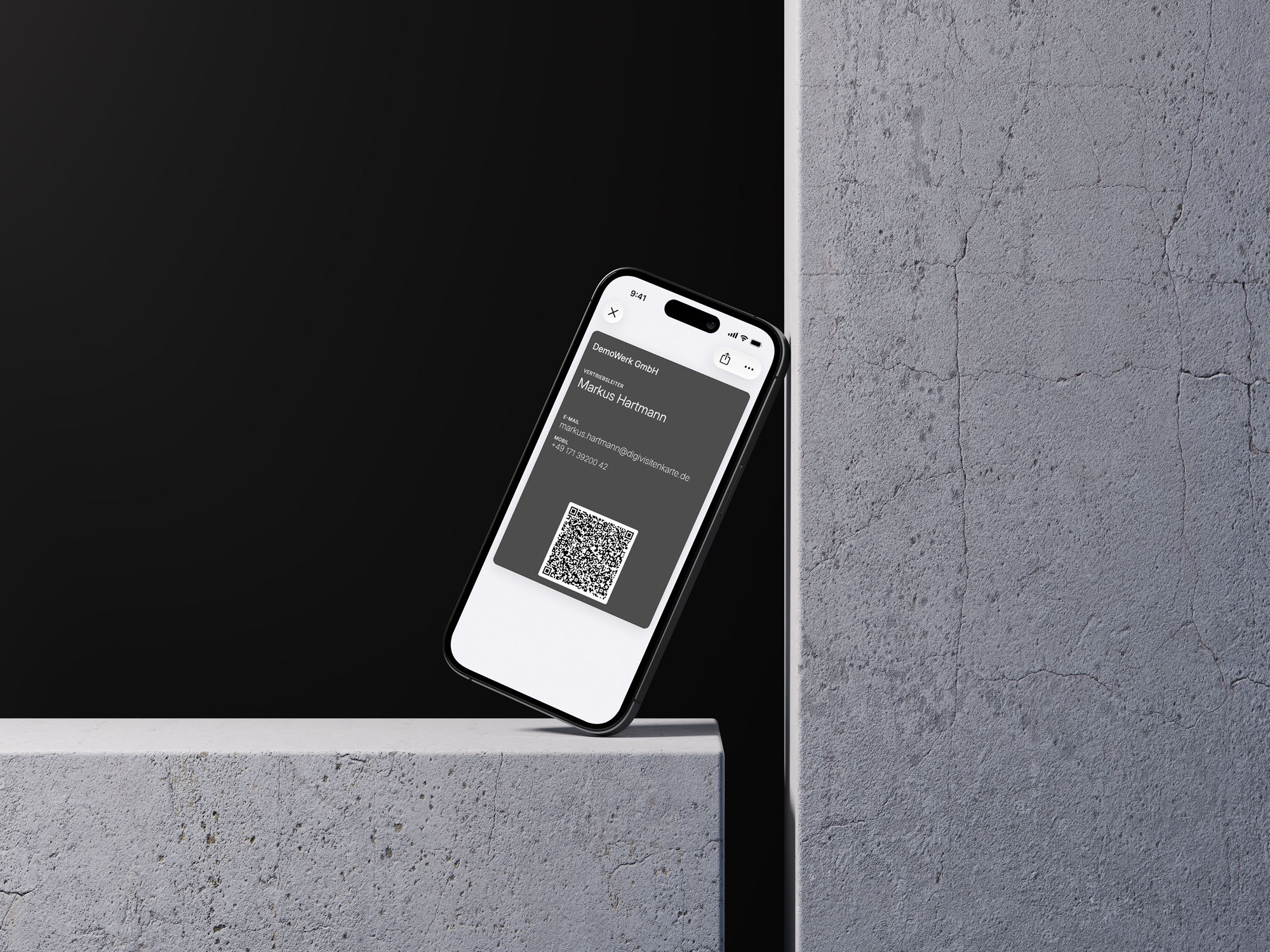 Ein iPhone auf dunklem Hintergrund zeigt eine graphitfarbene digitale Visitenkarte im Apple Wallet für Markus Hartmann, Vertriebsleiter, mit Kontaktdaten und einem scannbaren QR-Code